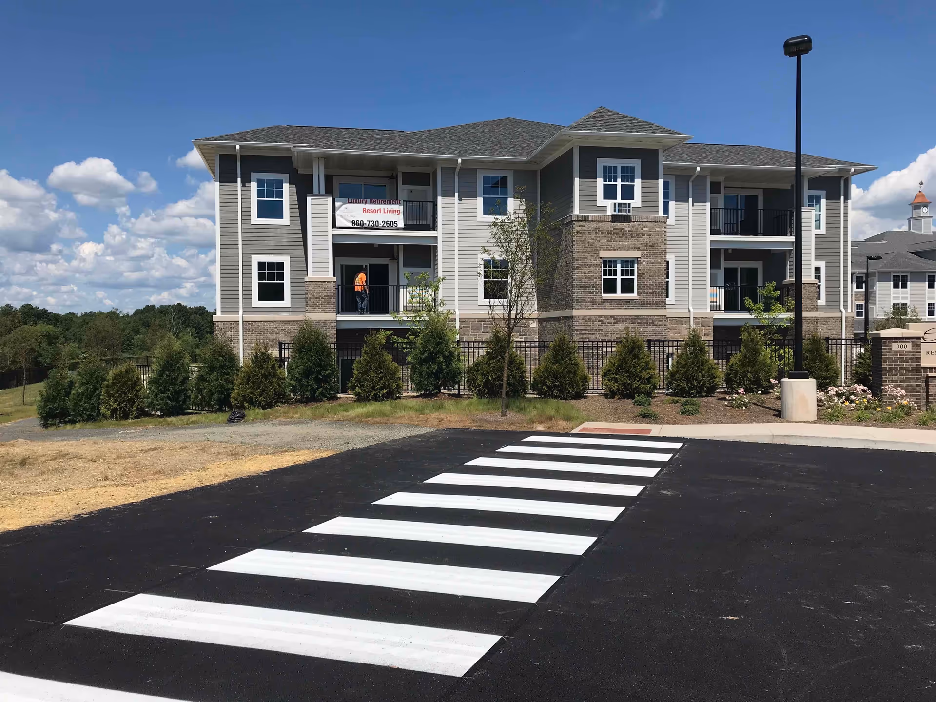 A modern multi-story senior living building with balconies and a crosswalk in front.