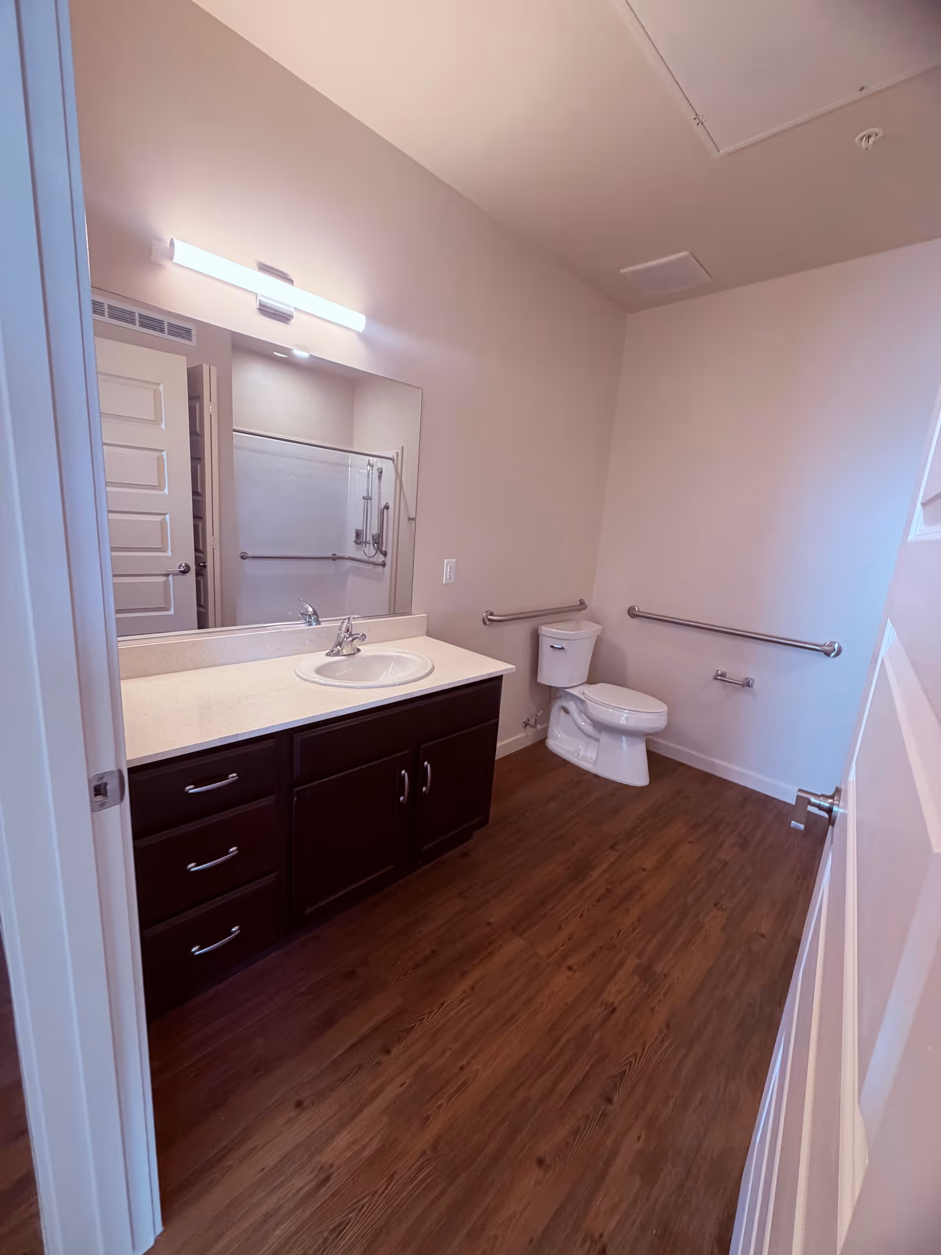 Accessible bathroom with dark wood vanity, mirror, sink, toilet, and grab bars.