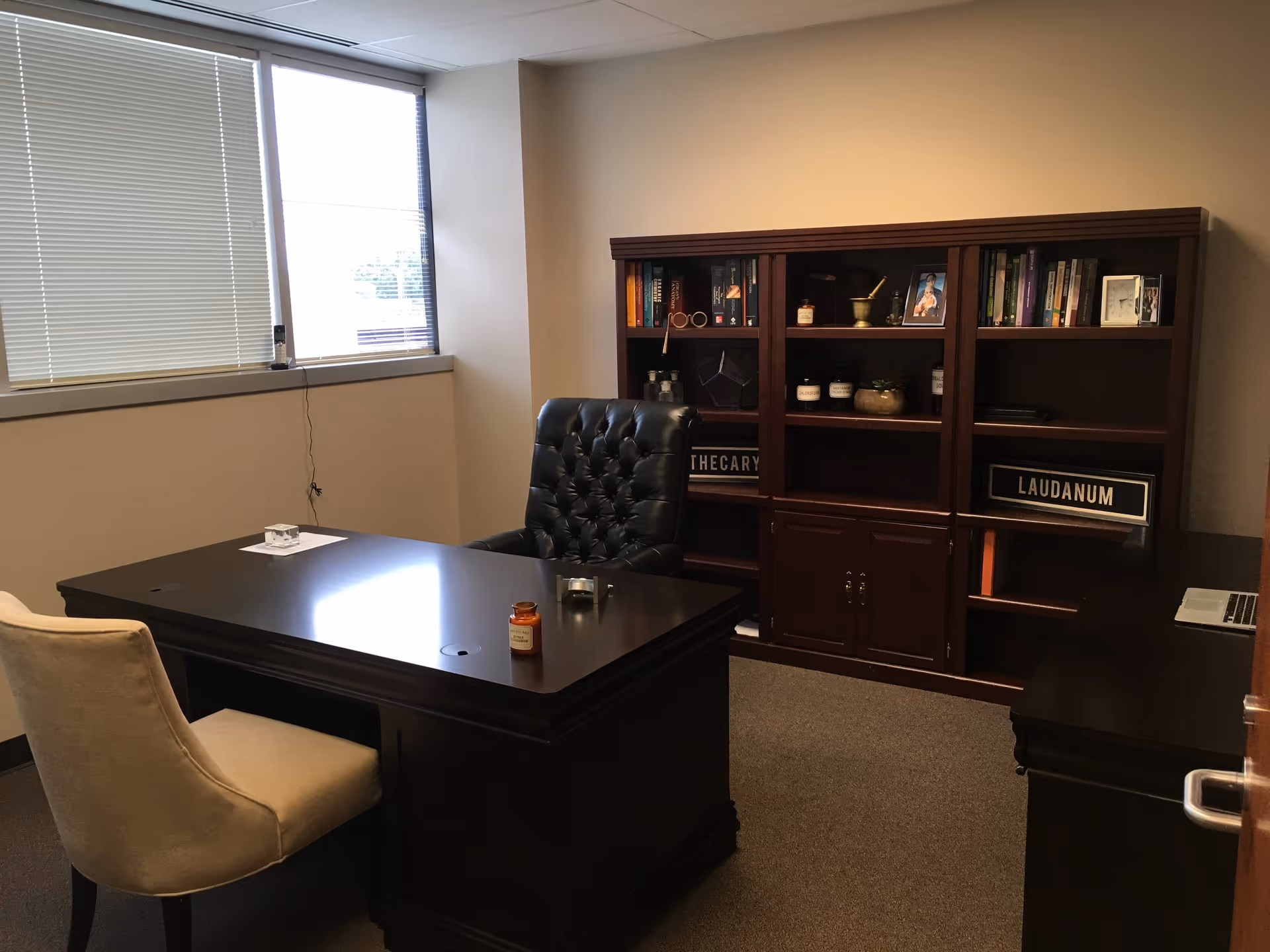 A dark wood desk with a tufted chair sits in an office with a large bookshelf.