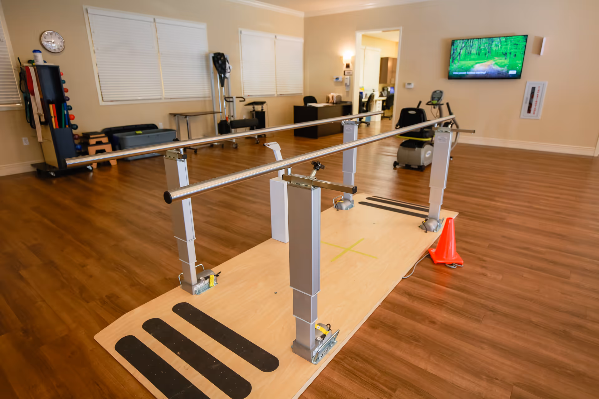 Rehabilitation gym with parallel bars, wooden floor, and exercise equipment in a facility.