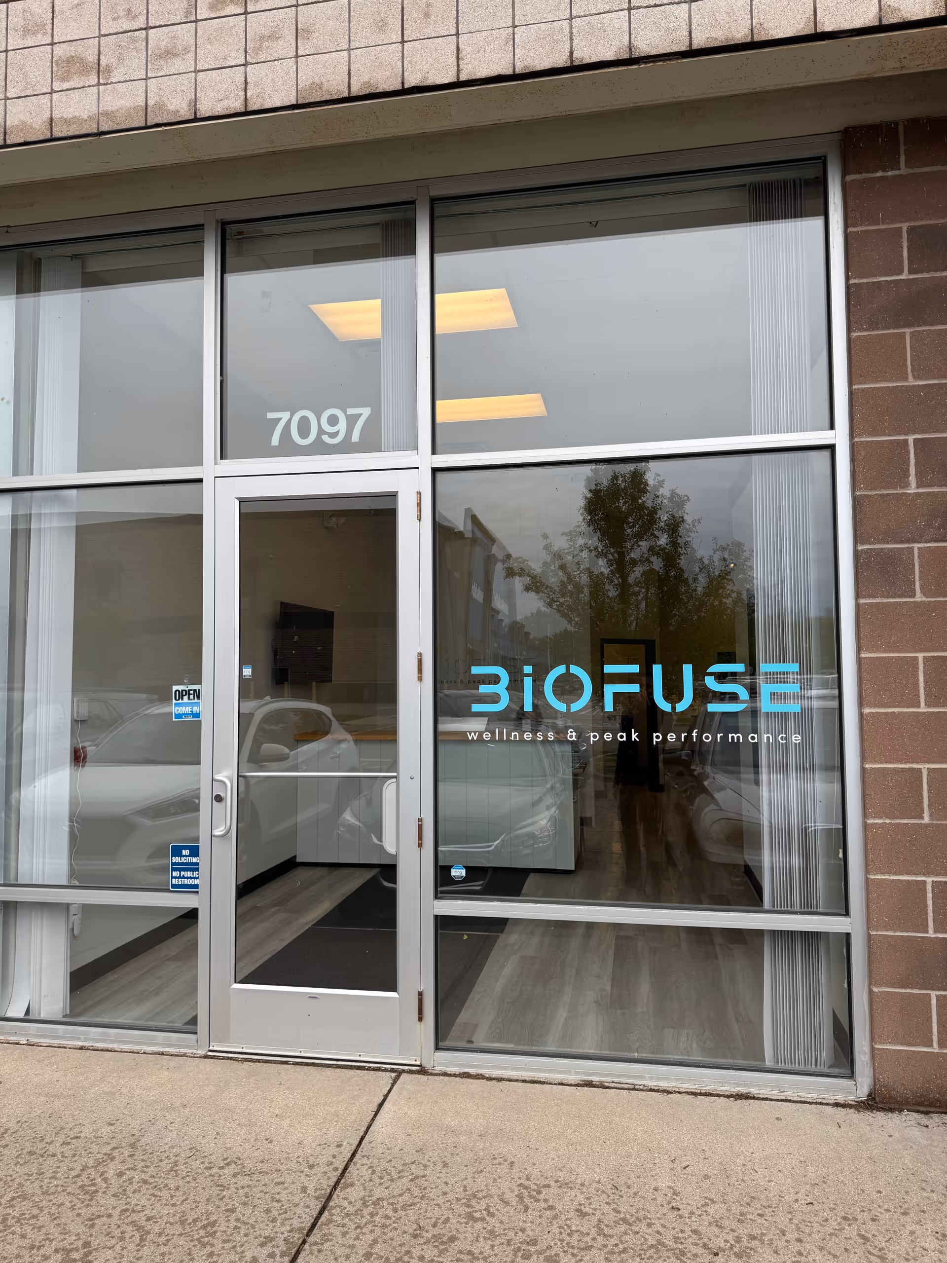 Glass storefront entrance with Biofuse logo and street number 7097 on brick facade.