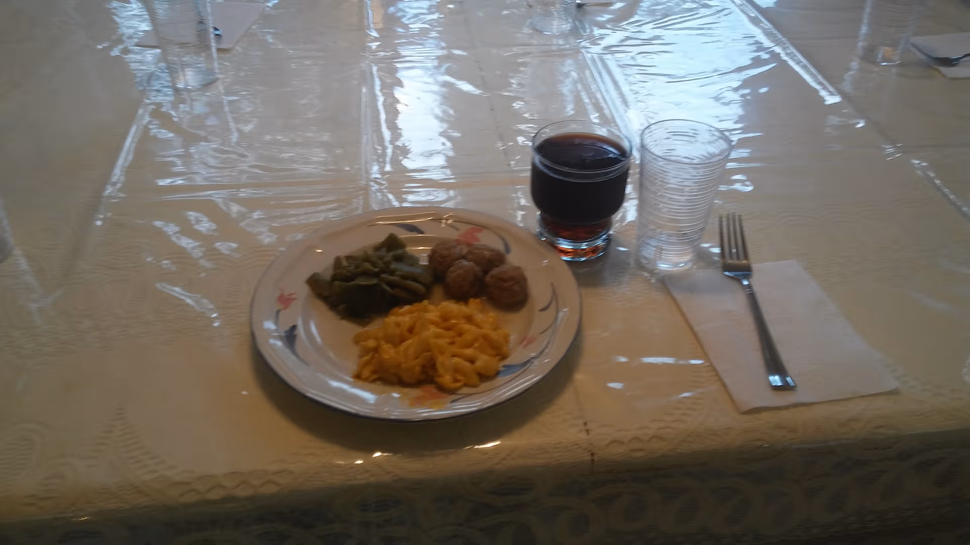 Plate with greens, meatballs, and pasta beside a glass of wine.