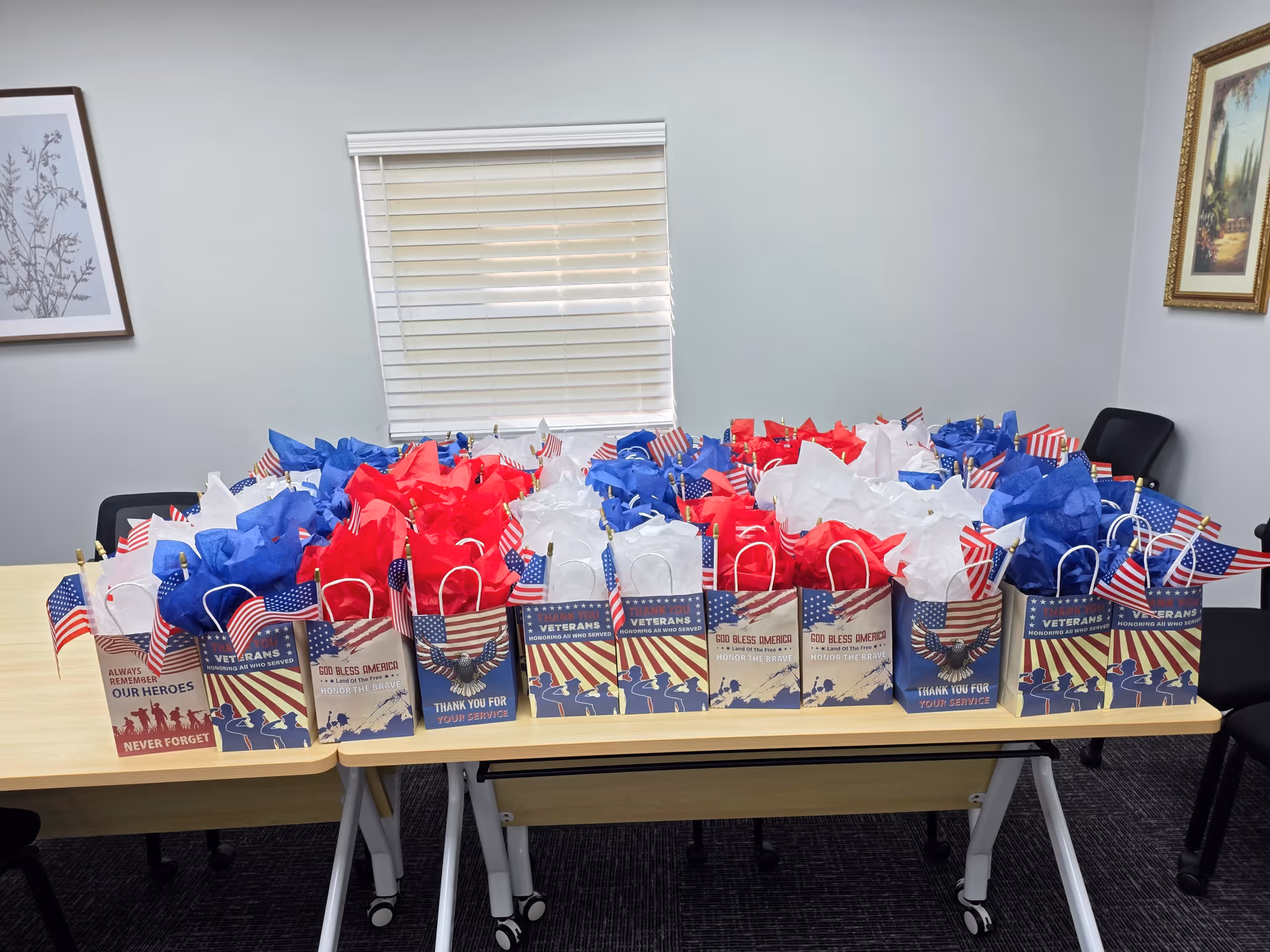 Table filled with red, white, blue gift bags with American flags in a quiet meeting room.