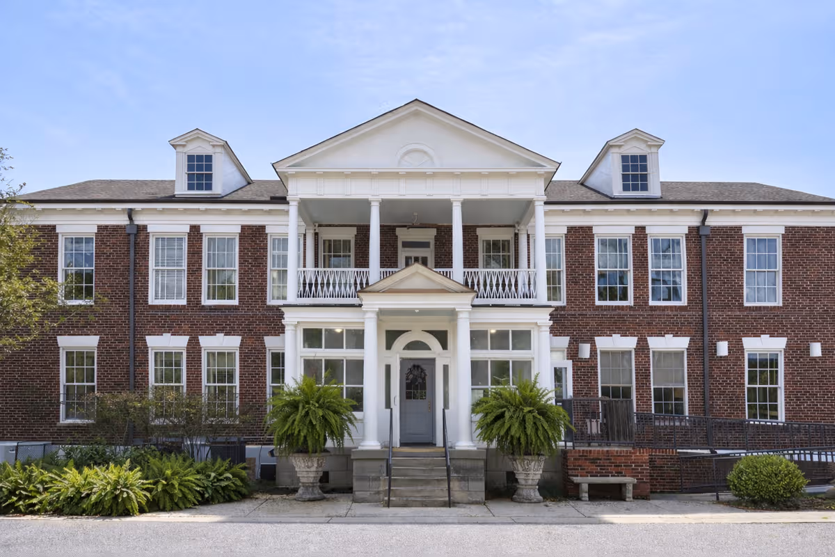 Brick senior living facility with white columns, central portico, and symmetrical windows.