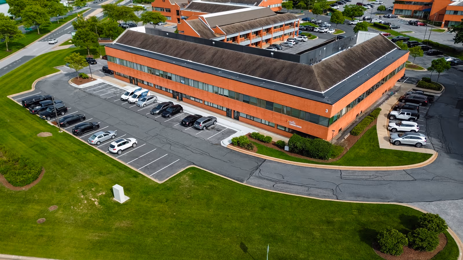Aerial view of a brick senior living facility with a parking lot and surrounding green space