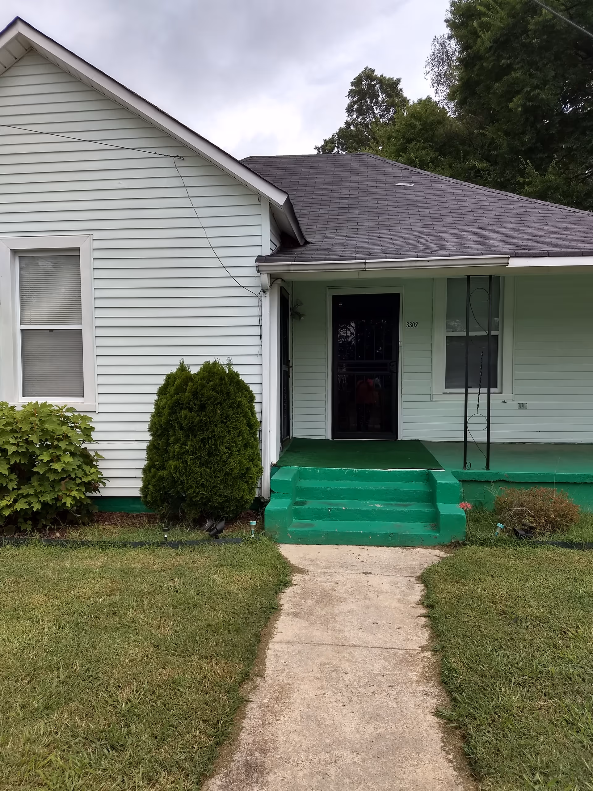 Exterior view of a small light-blue building with green steps and entrance.