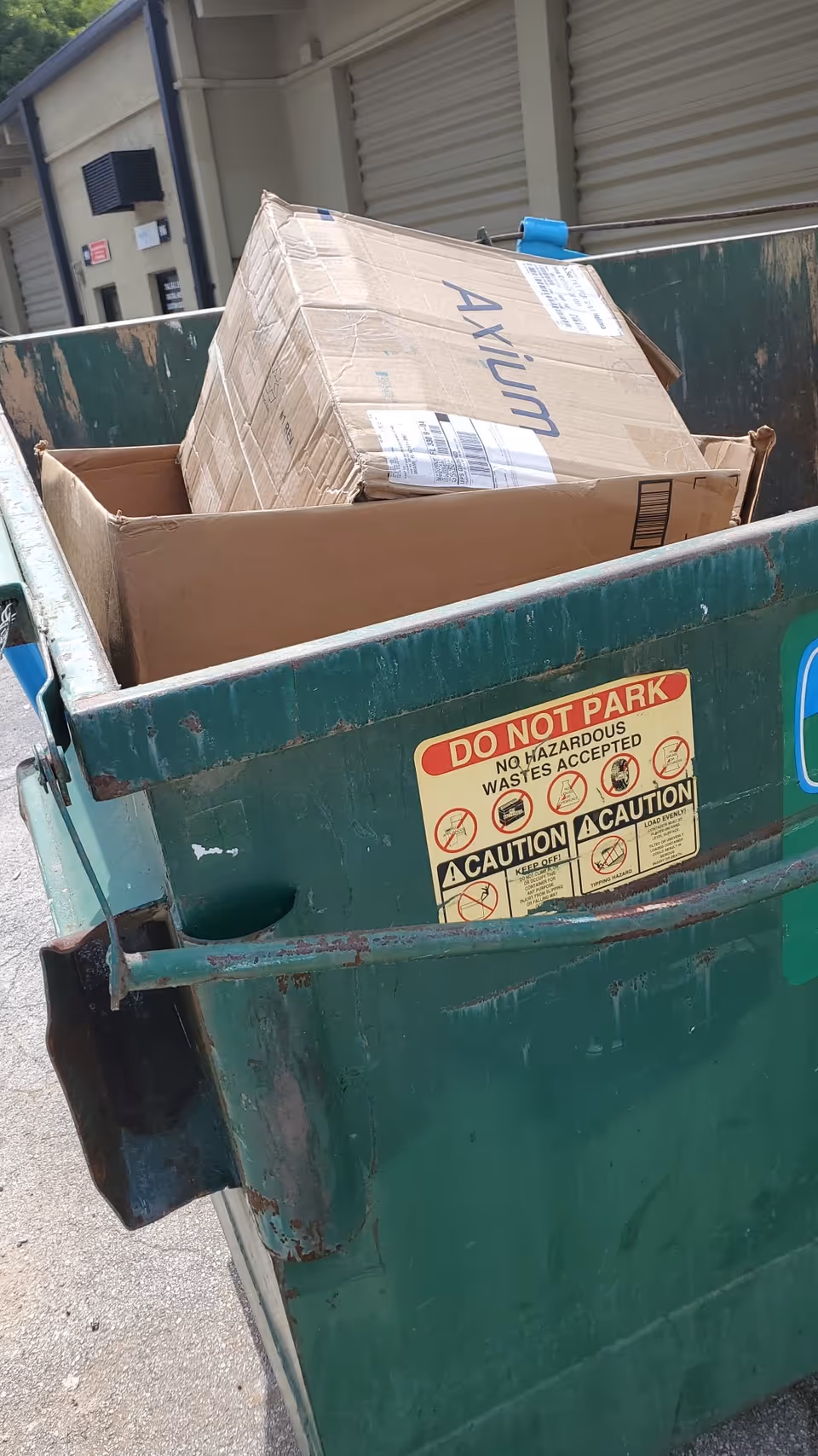 Green dumpster overflowing with cardboard boxes outside Fountain Manor Health & Rehabilitation Center.