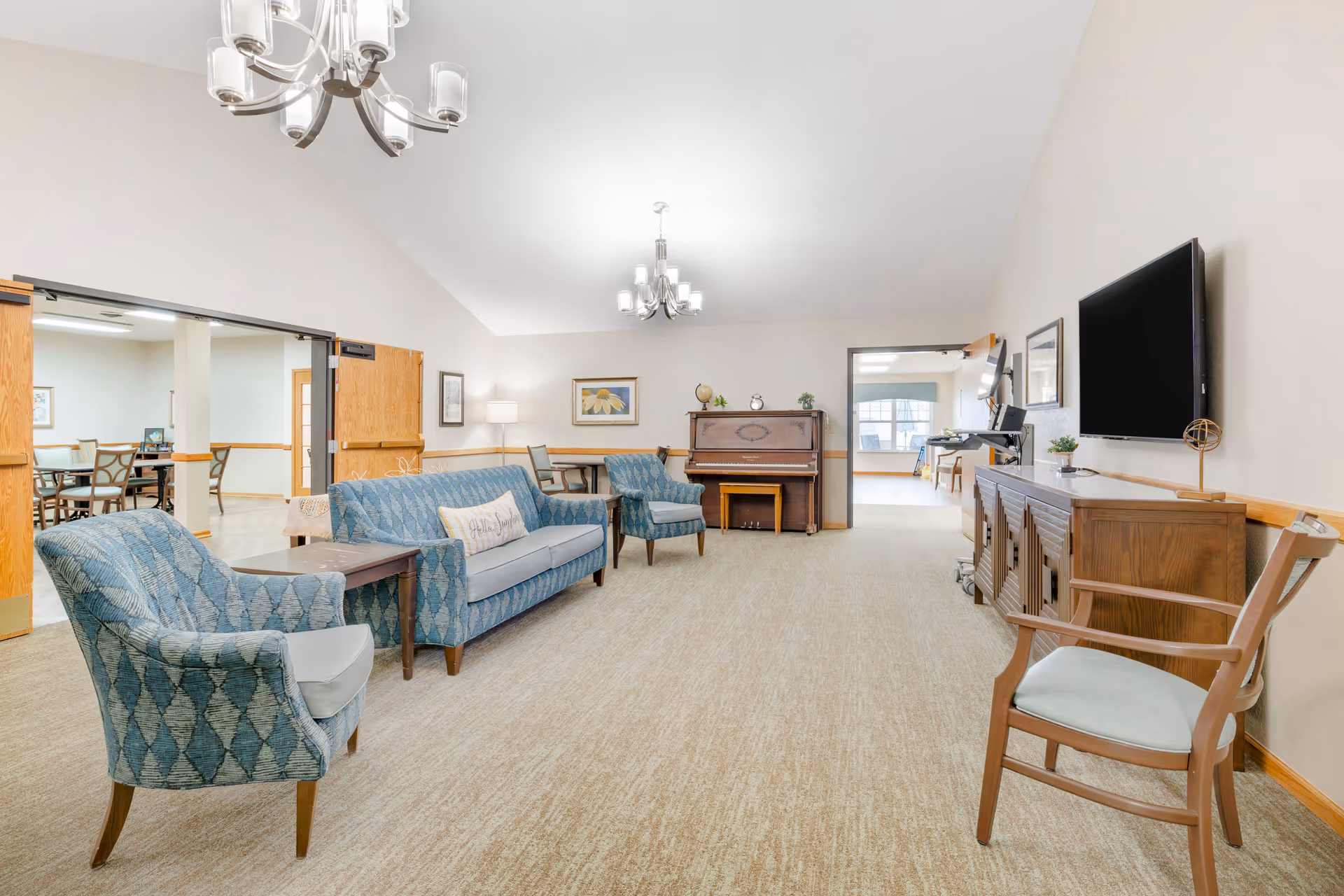 Spacious lounge in a Noelitz Home facility with blue sofas, piano, and a TV.