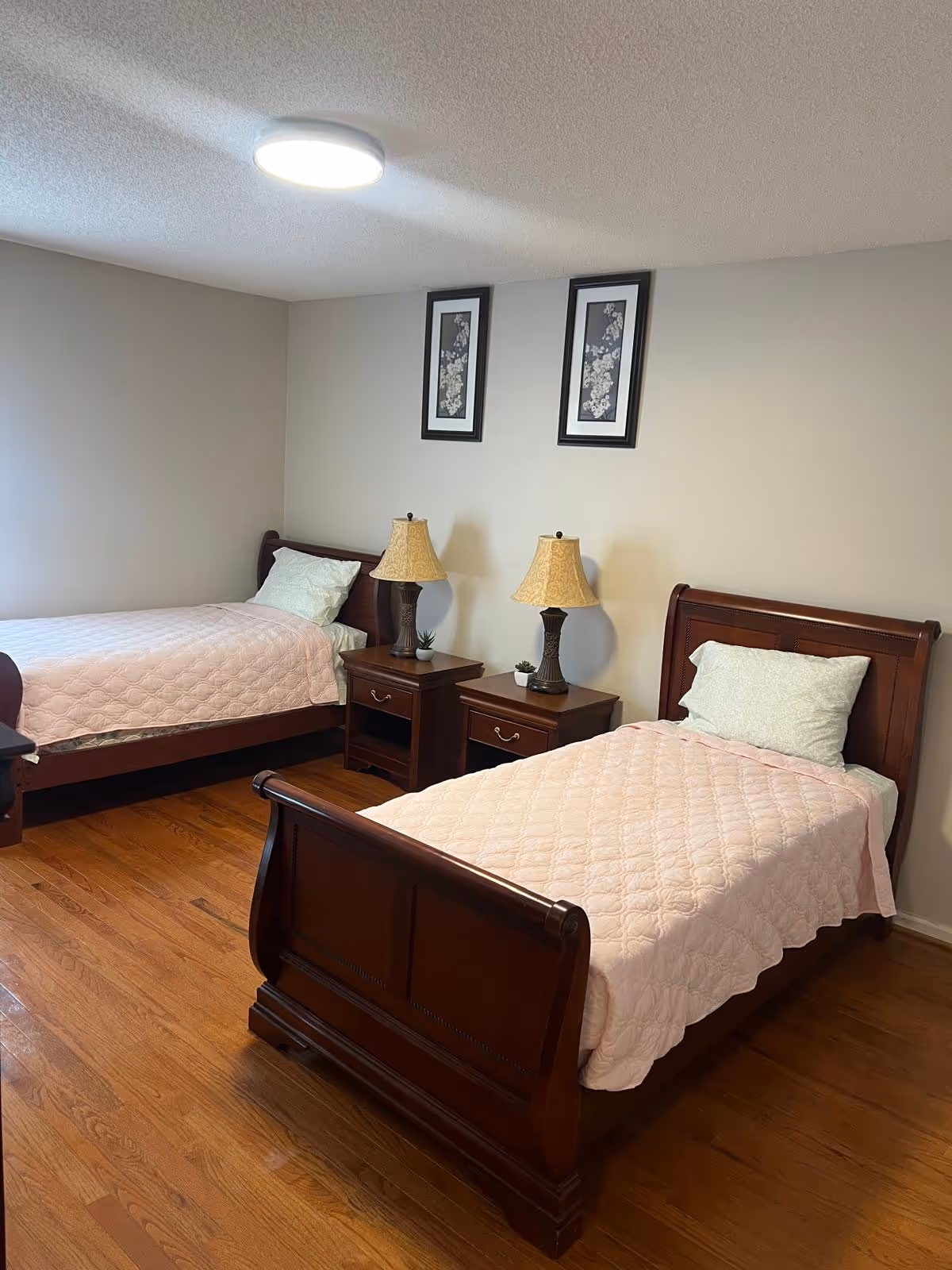 Two single beds with matching quilts, nightstands, lamps, and framed artwork in a tidy bedroom.
