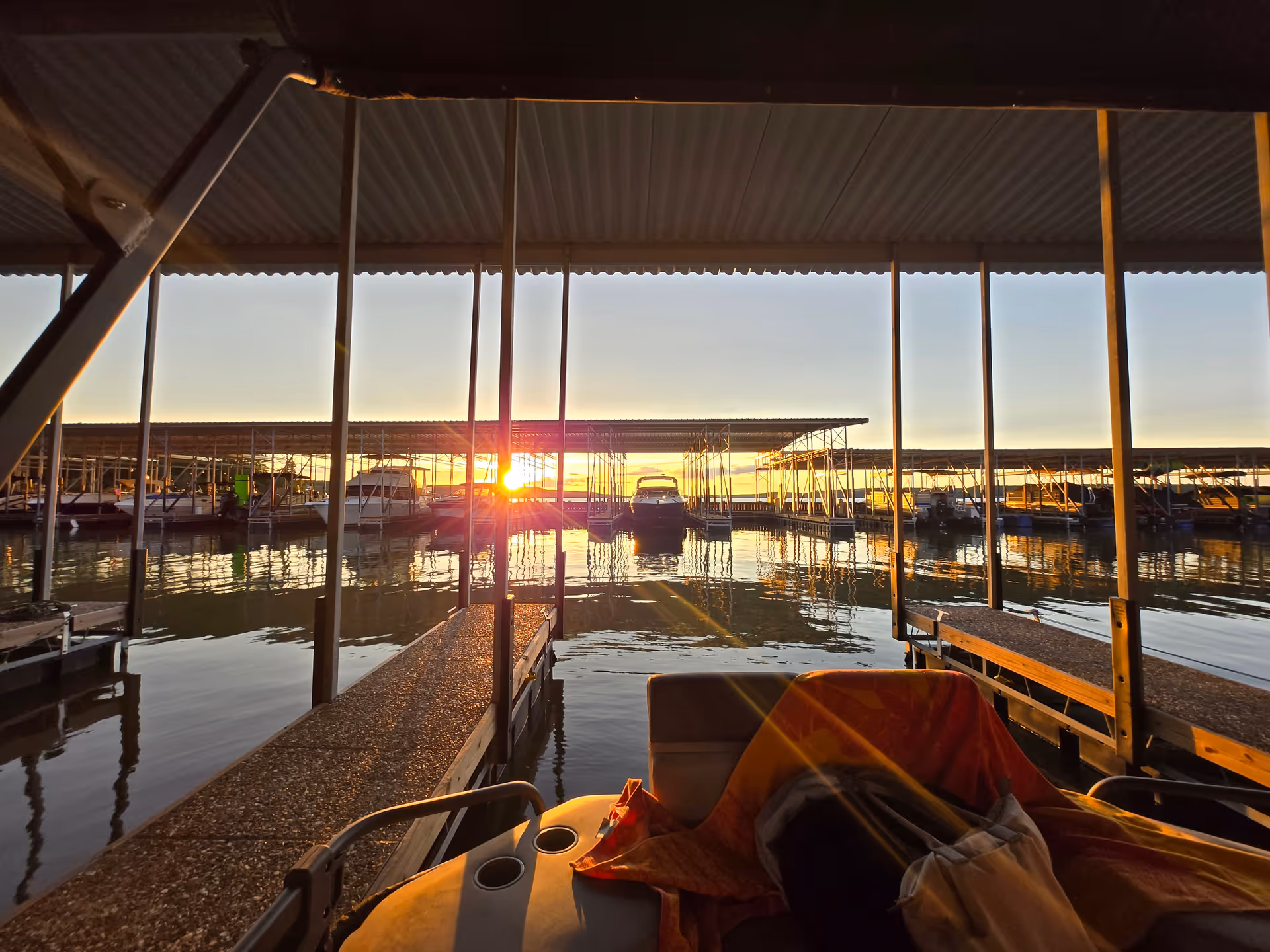 Sunset over a covered marina with boat slips and calm water reflections.