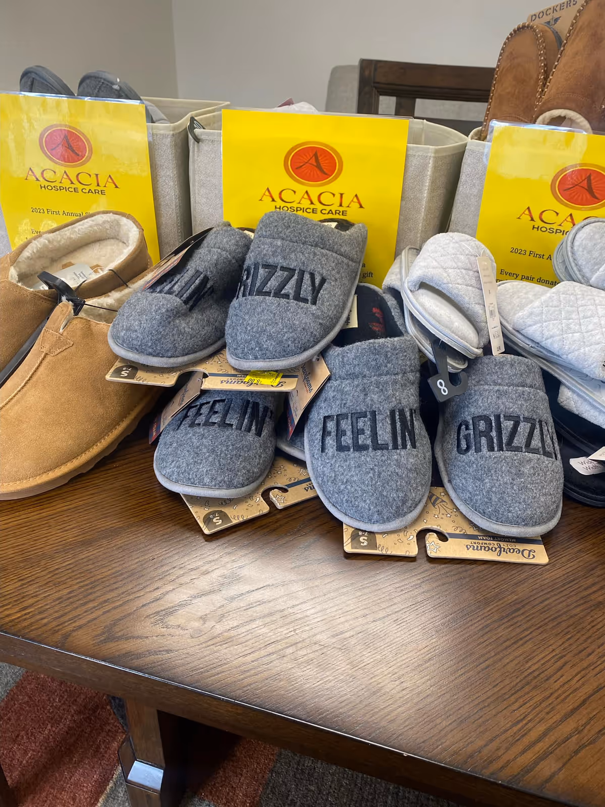 Assorted hospice slippers and Acacia gift boxes arranged on a table.