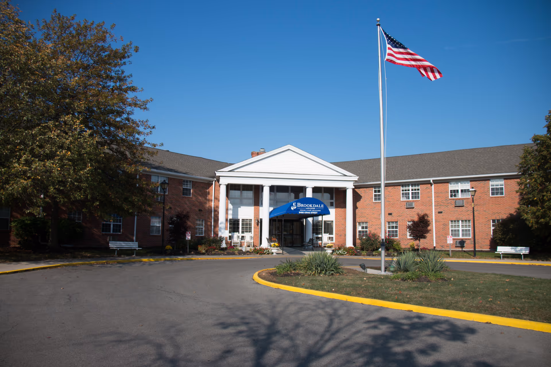 Brick senior living building with front entrance, blue Brookdale canopy, flagpole, and circular driveway.