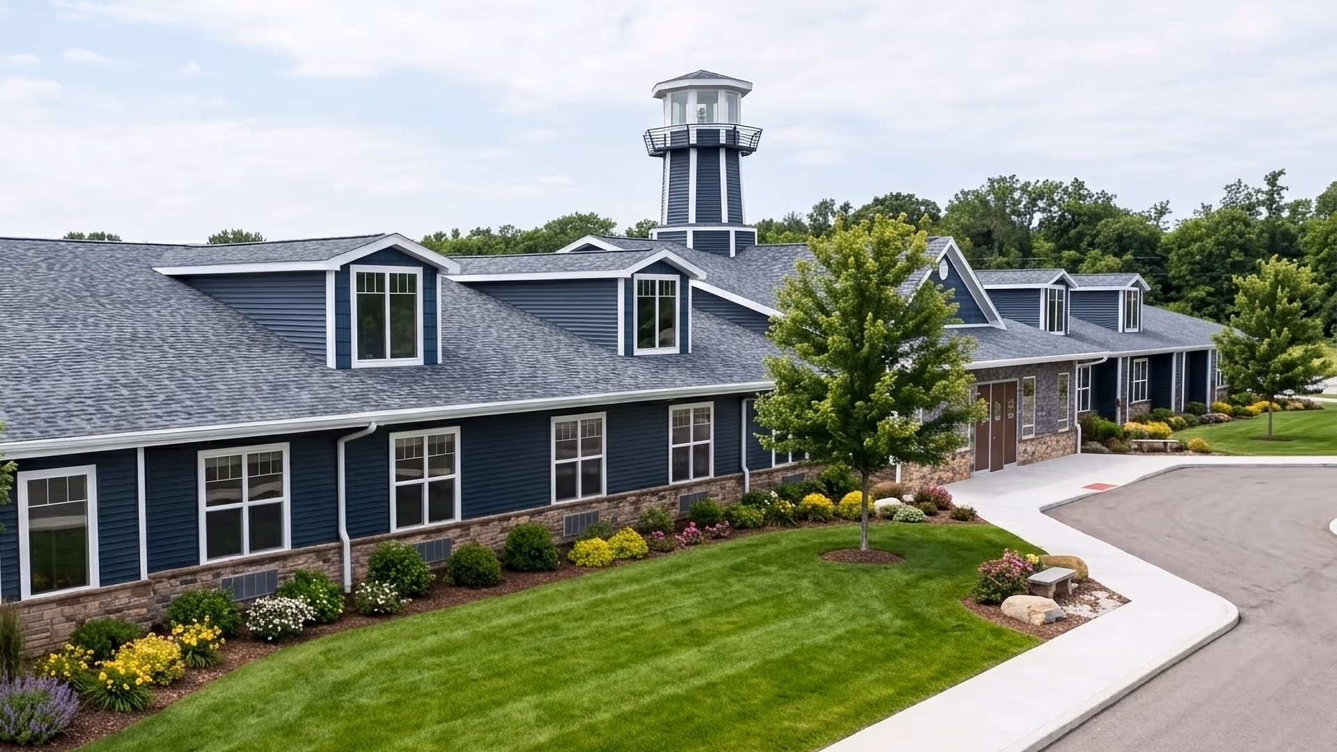 Blue senior living facility with stone base, landscaped lawn, and curved driveway.