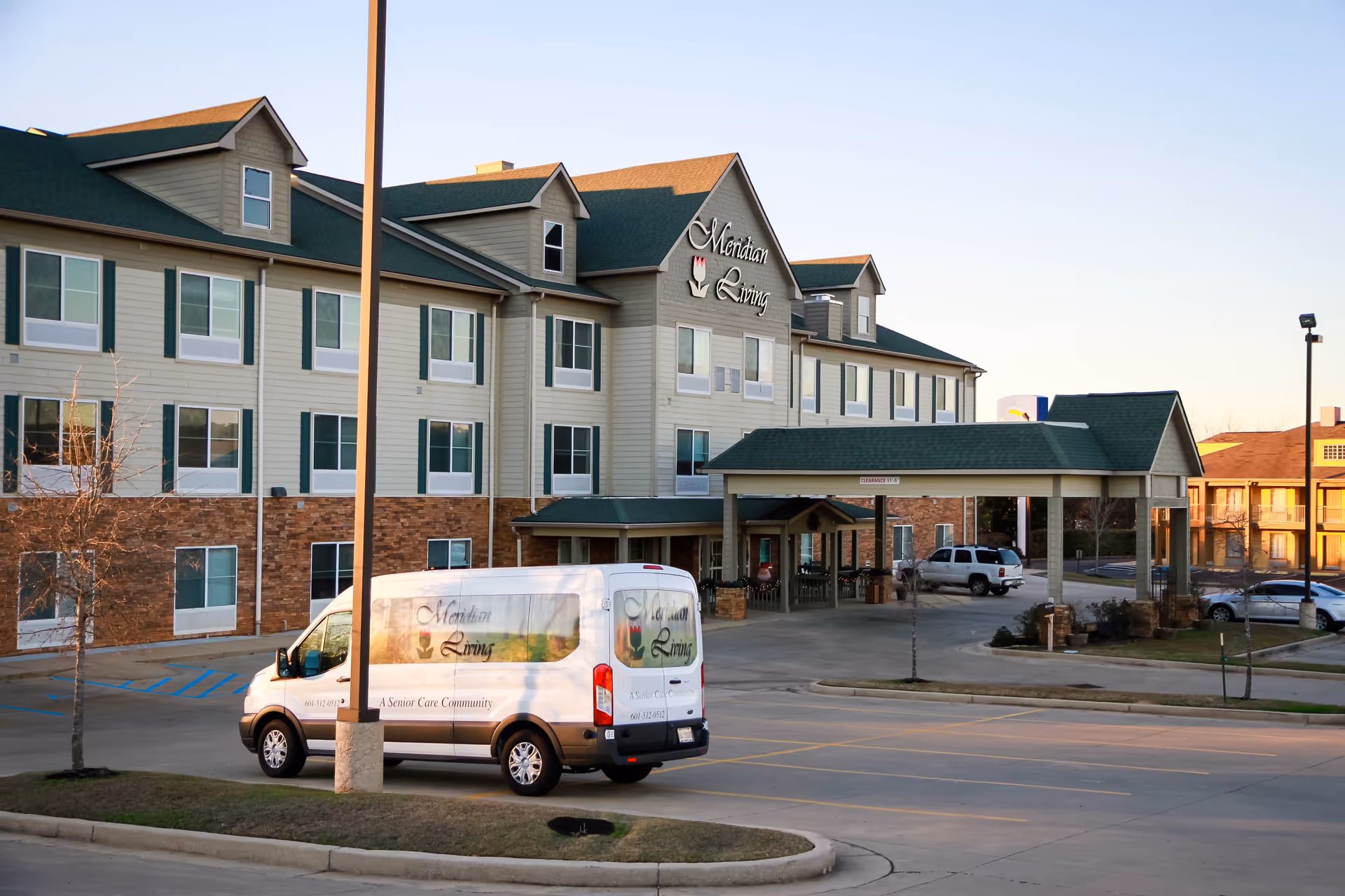 Exterior view of Meridian Living senior care community building with a parked Meridian Living van in the foreground and a covered entrance area.