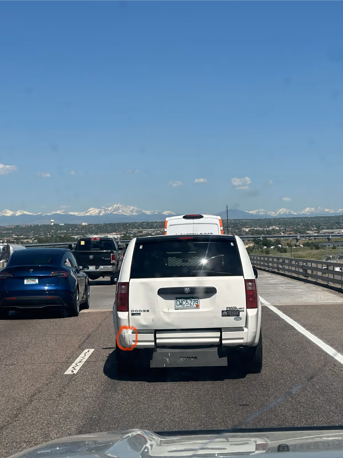 Cars travel on a highway with a white SUV centered and mountains in the distance.