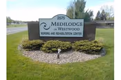 Exterior view of a Medilodge of Westwood sign surrounded by rocks and trimmed shrubs.