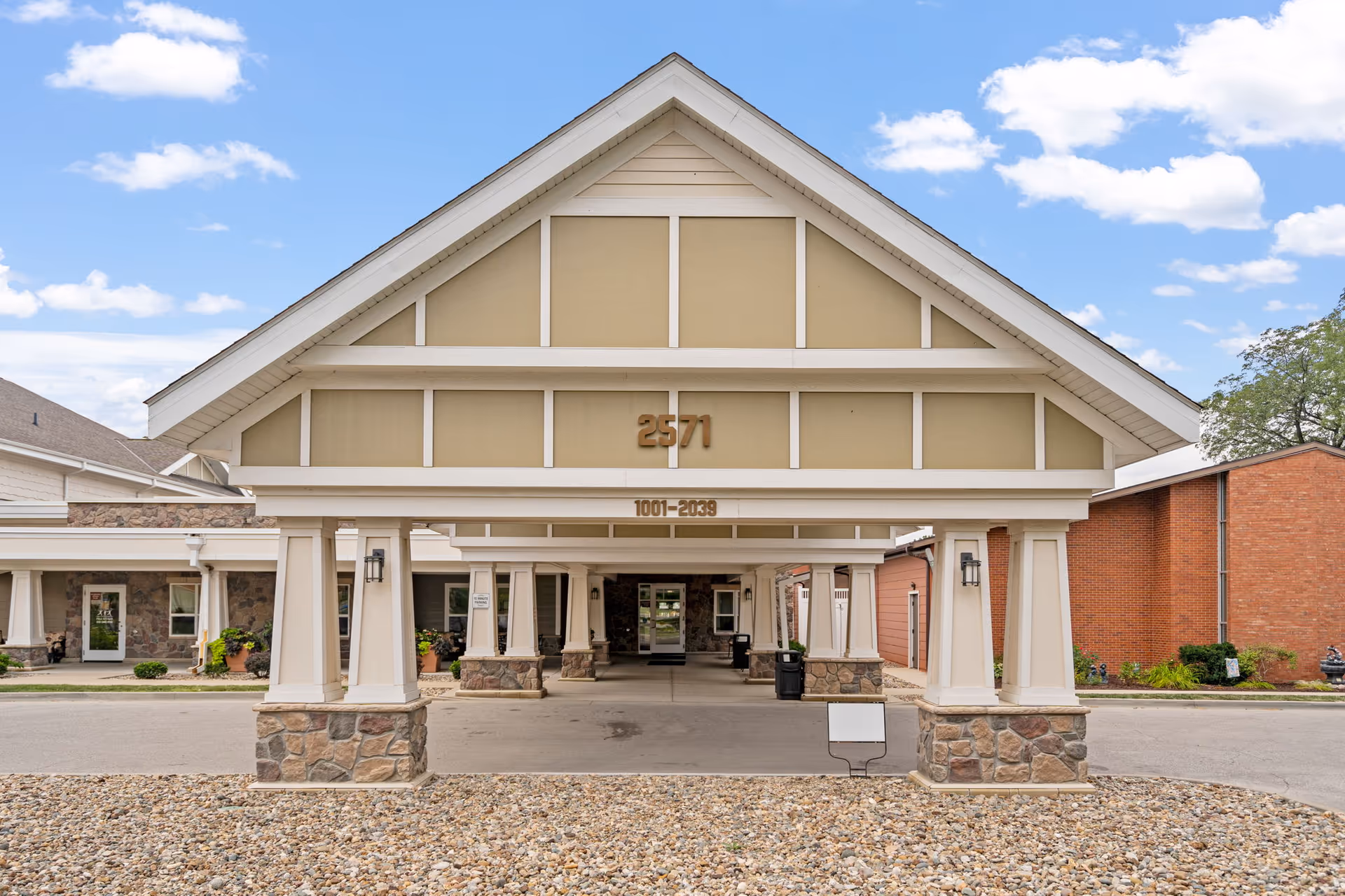 Front entrance of a senior living facility with a large porte-cochere and stone bases.
