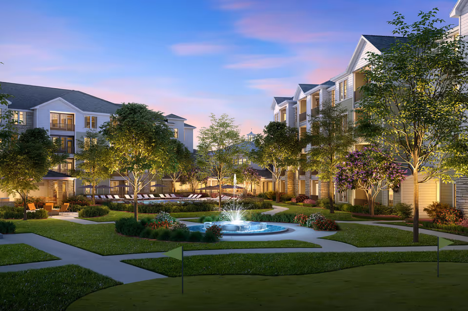 Outdoor courtyard of a senior living community with a central fountain, pathways, trees, and buildings.