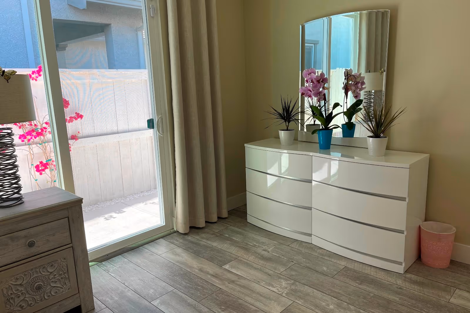 White curved dresser with mirror and potted plants beside a glass sliding door.