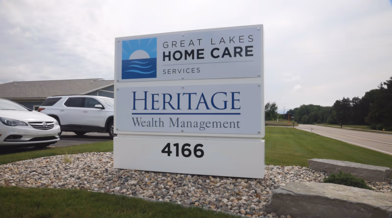 A two-tier sign displays Great Lakes Home Care Services and Heritage Wealth Management at a curb.