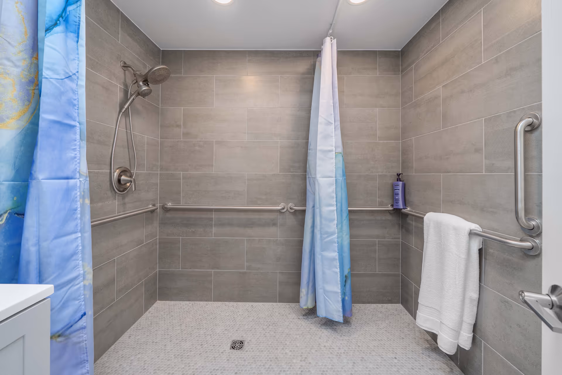 Accessible tiled bathroom with a shower, curtains, grab bars, and a towel rack.