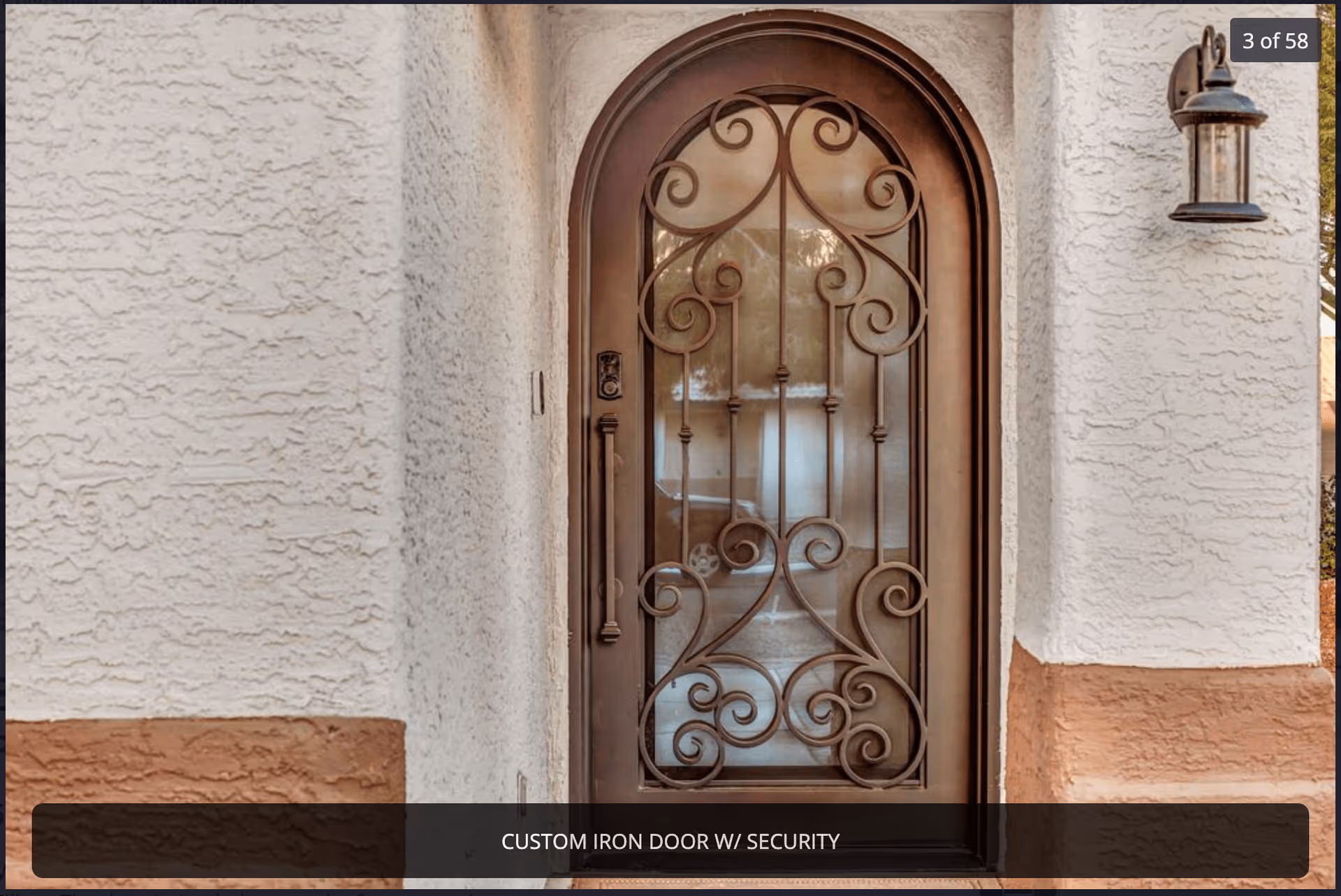 Arched decorative iron security door set in a stucco exterior entryway.