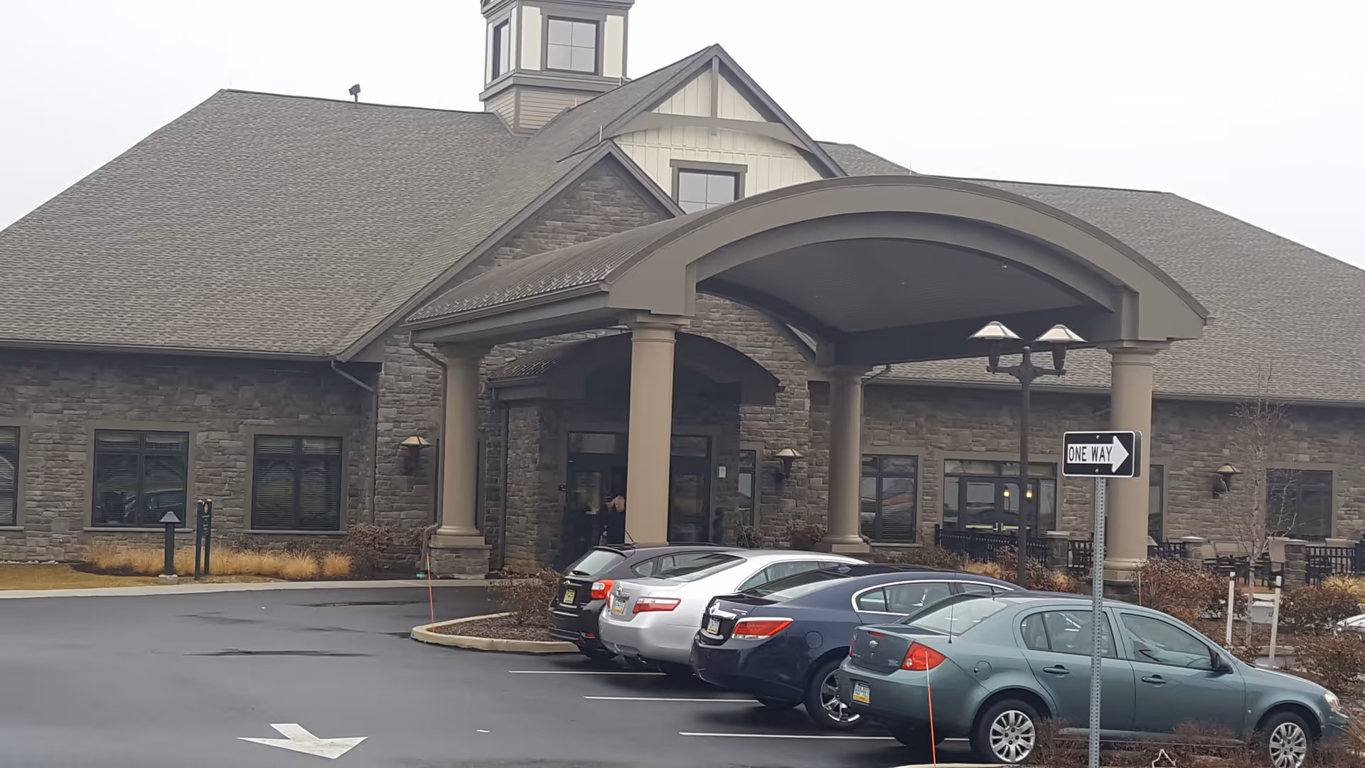 Stone retirement community entrance with arched canopy and parked cars outside