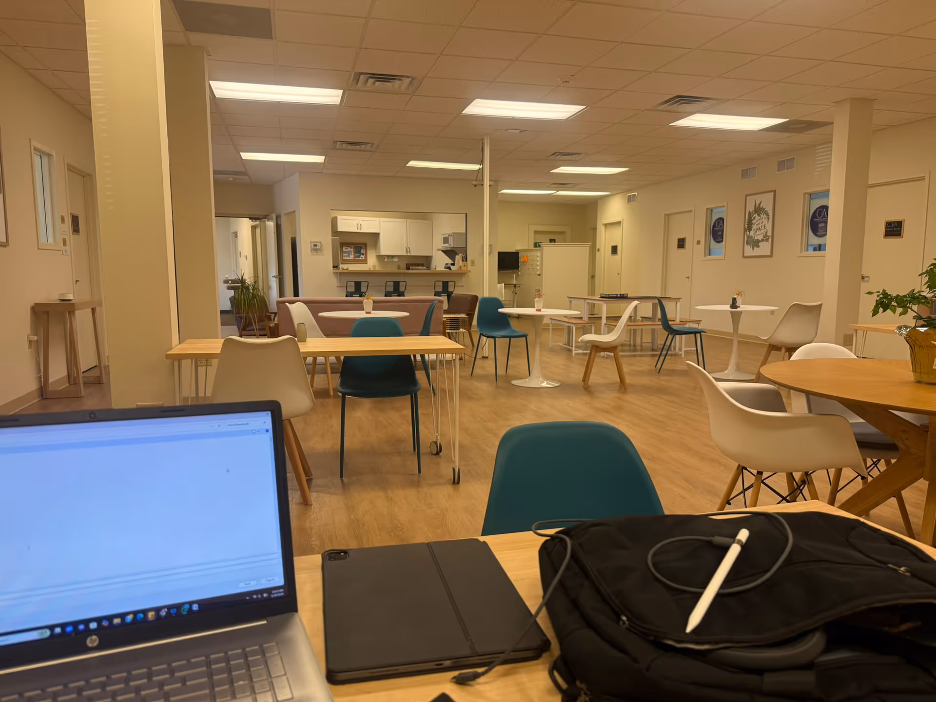 Bright senior living dining area with tables, chairs, and a kitchenette in the background.