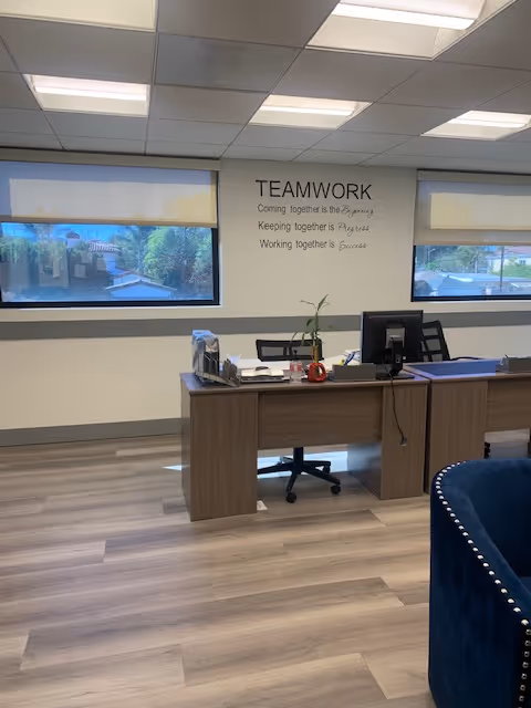 Office reception area featuring desk, computer, plant, and TEAMWORK wall sign.
