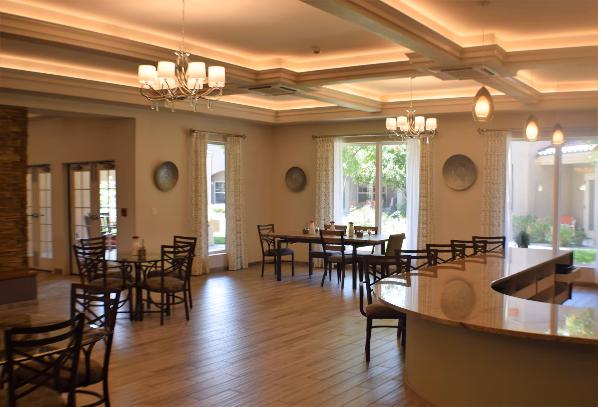 Bright interior dining area with tables, chairs, chandeliers, and a curved countertop.