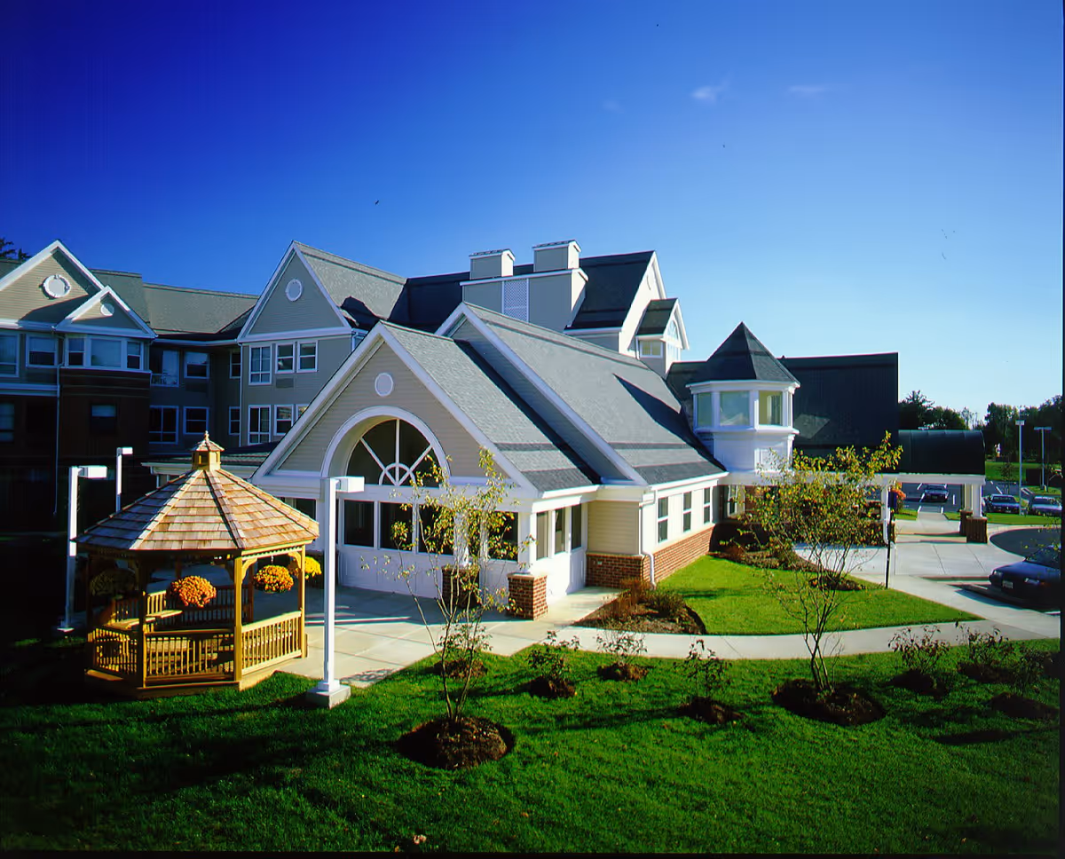 Front exterior of a multi-story senior living building with a gazebo, manicured lawn, and a covered entrance.