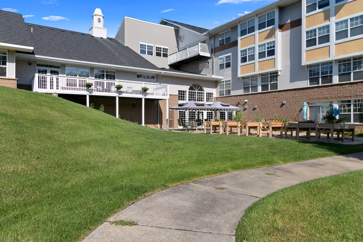 Exterior view of St. Andrew’s Village showing a grassy courtyard with a curved sidewalk, patio seating and raised planters in front of a multi-story building.