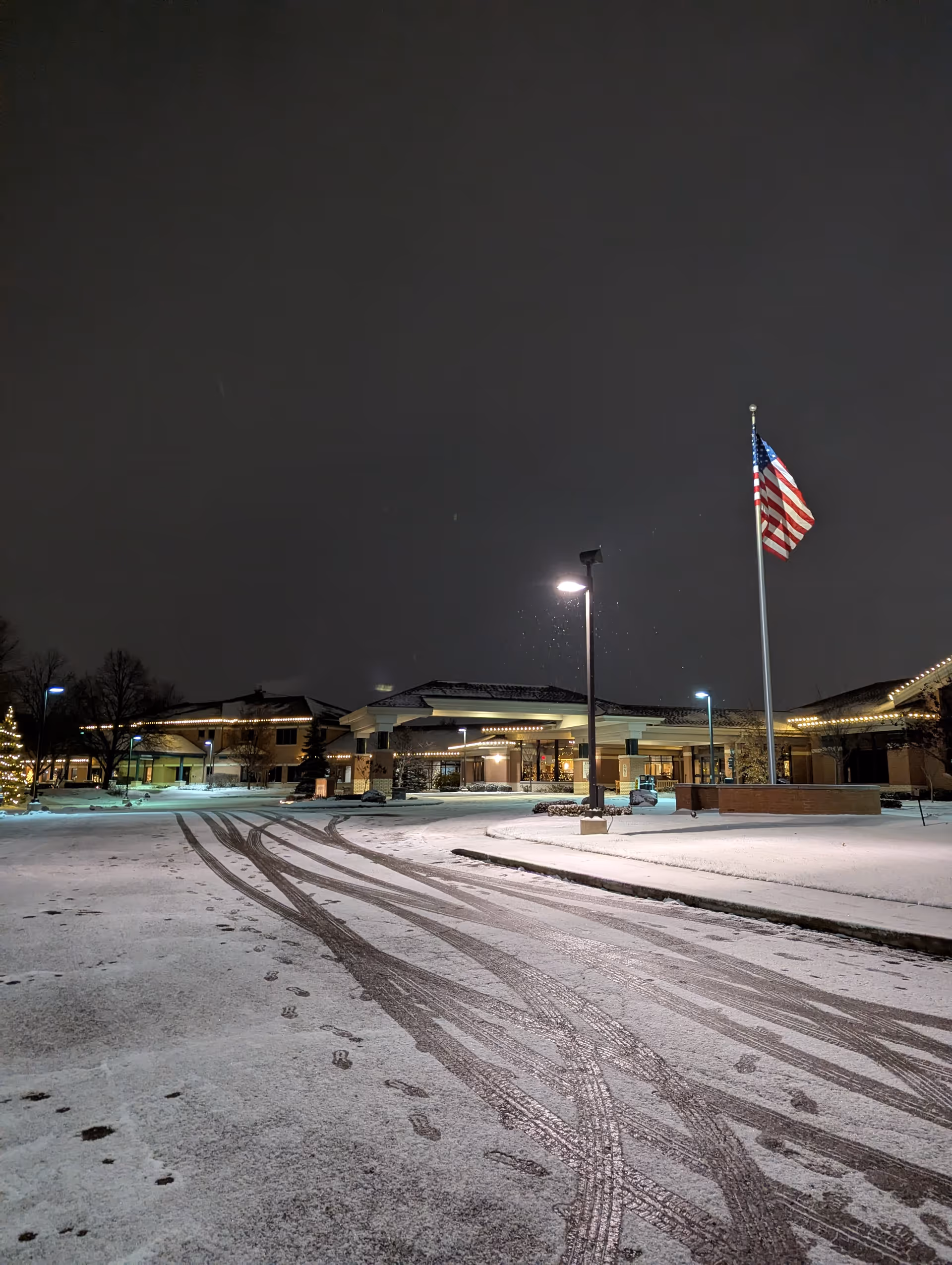 Night exterior of Angela Hospice facility with snow, a lit entrance, and an American flag.