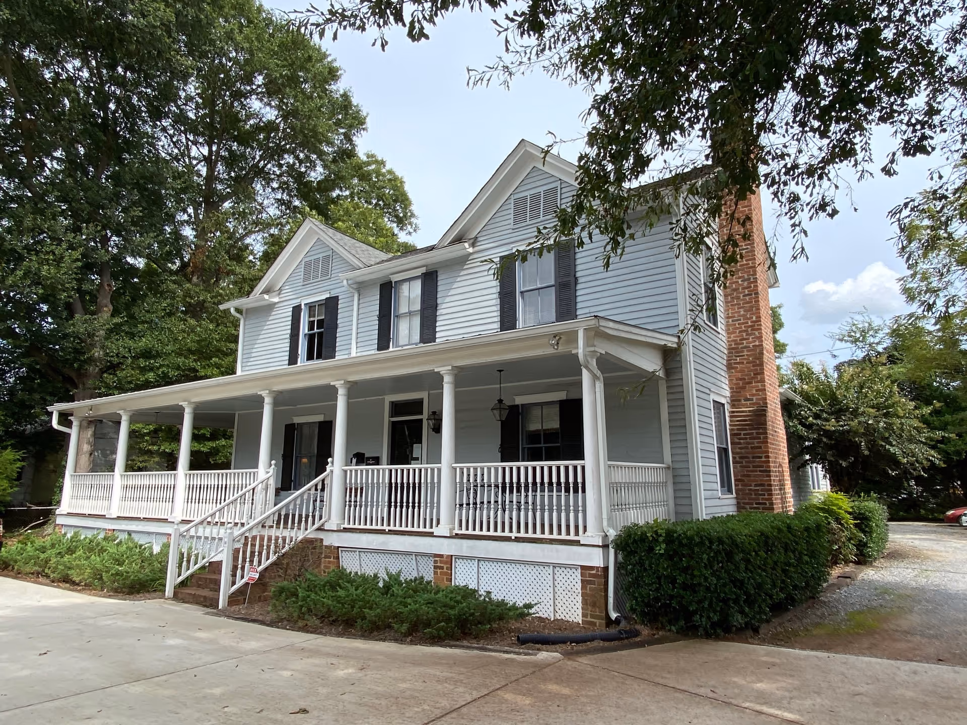 Historic two-story house with wraparound porch, white siding, and black shutters.