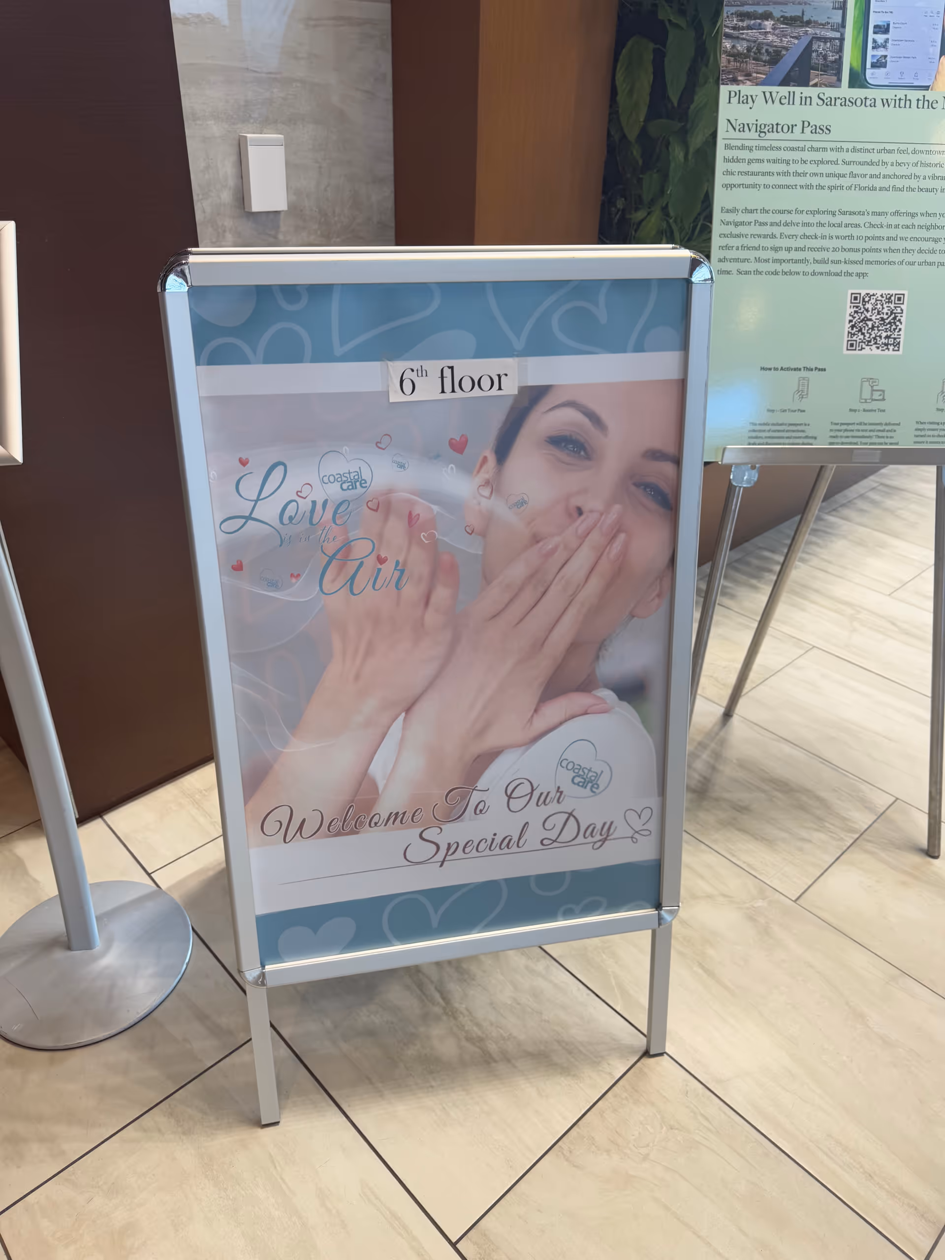 Poster sign on a stand in an interior lobby featuring a smiling woman.