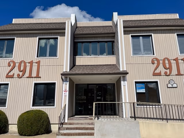 Two-story beige building with front entrance, stairs, shrubs, and Oasis Homecare Services signage.