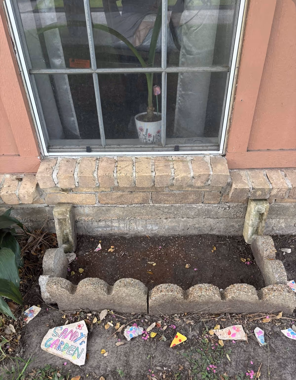 Outside Gracious Hearts Home Care, a brick wall with a window and small garden bed.