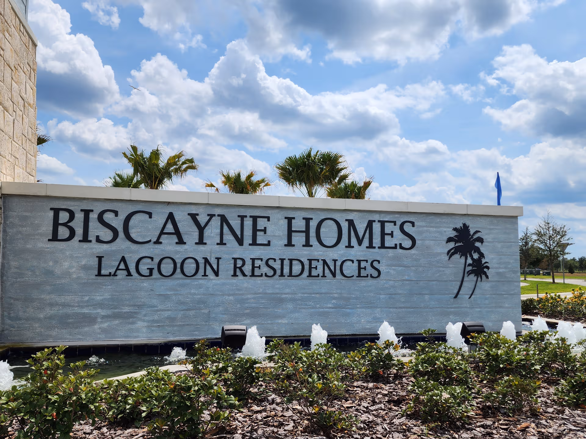 Large stone sign reading Biscayne Homes Lagoon Residences with palm trees and fountains.