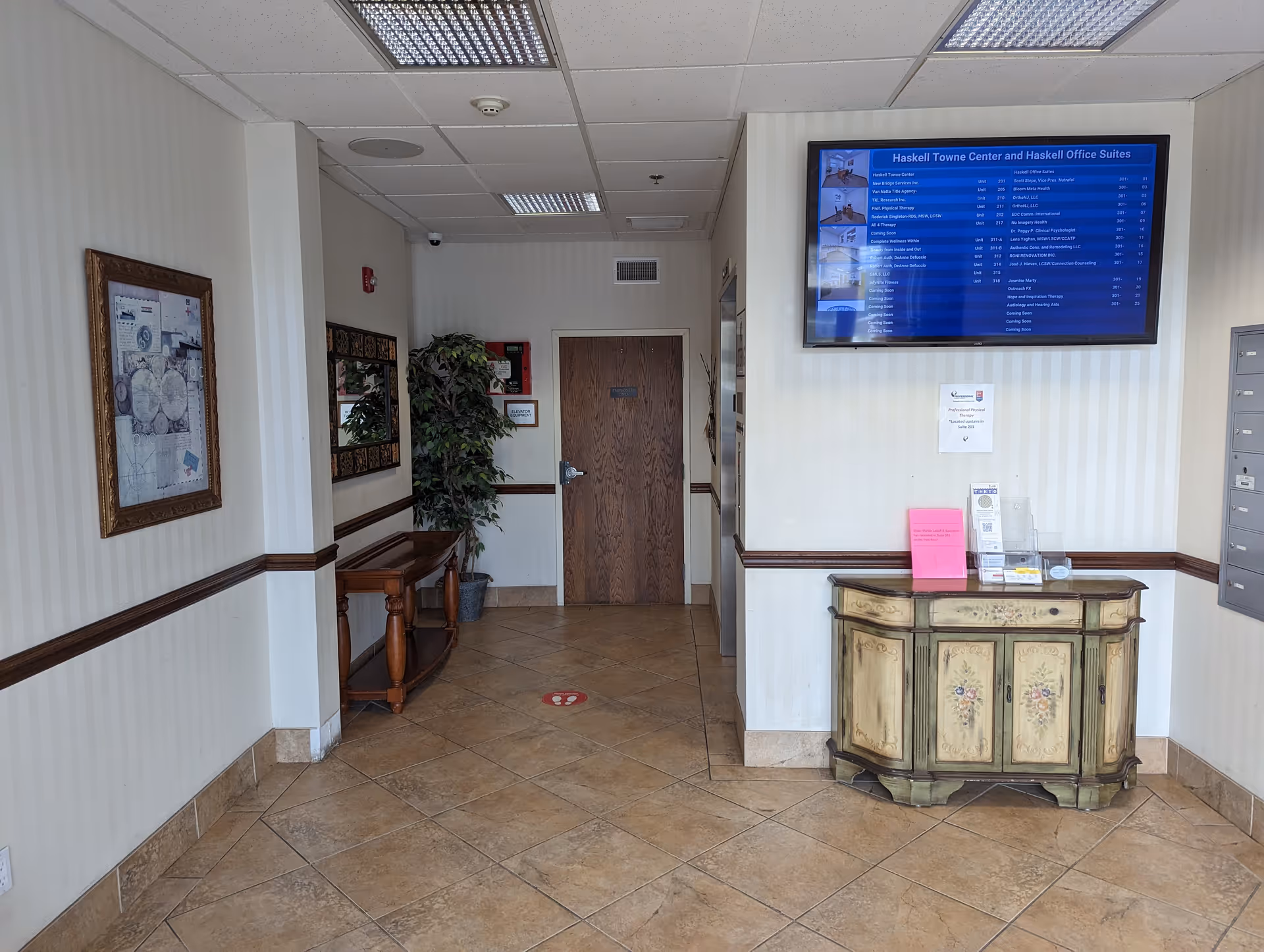 Interior hallway of a senior living facility with a decorative cabinet and mounted screen.