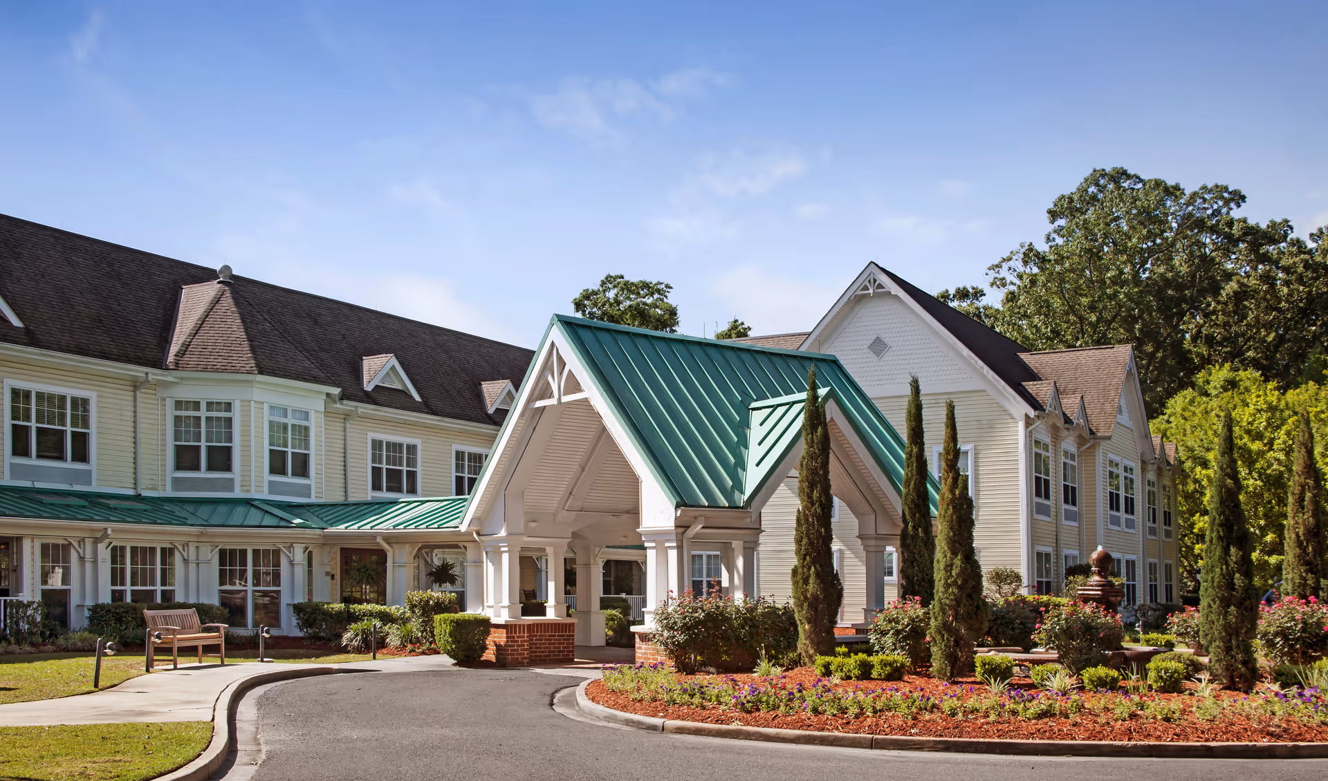 Exterior view of Sunrise of Baton Rouge with green-metal roof entrance and manicured landscaping.