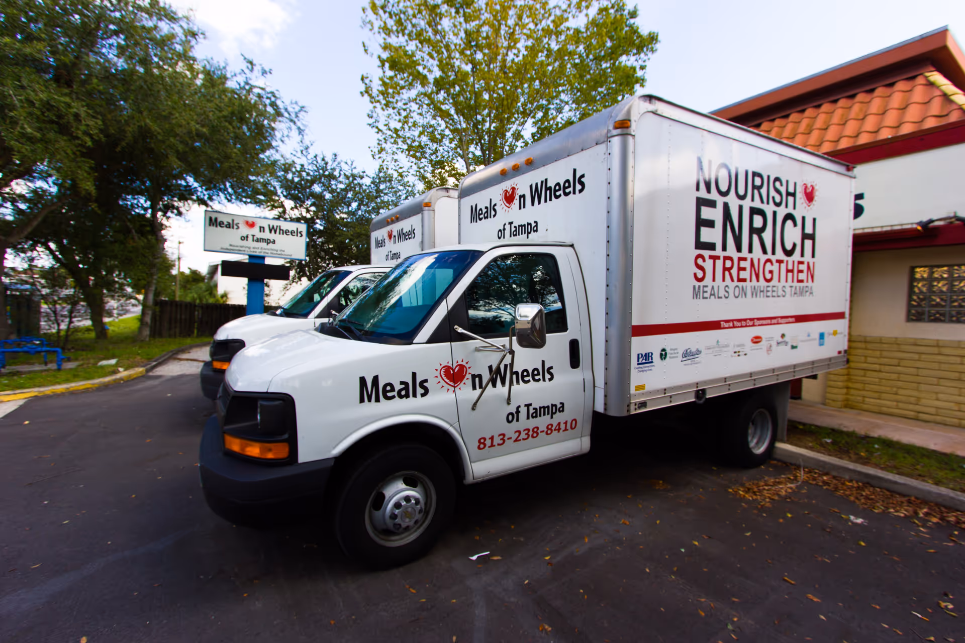 Two Meals on Wheels delivery trucks parked outside a facility, with signage.