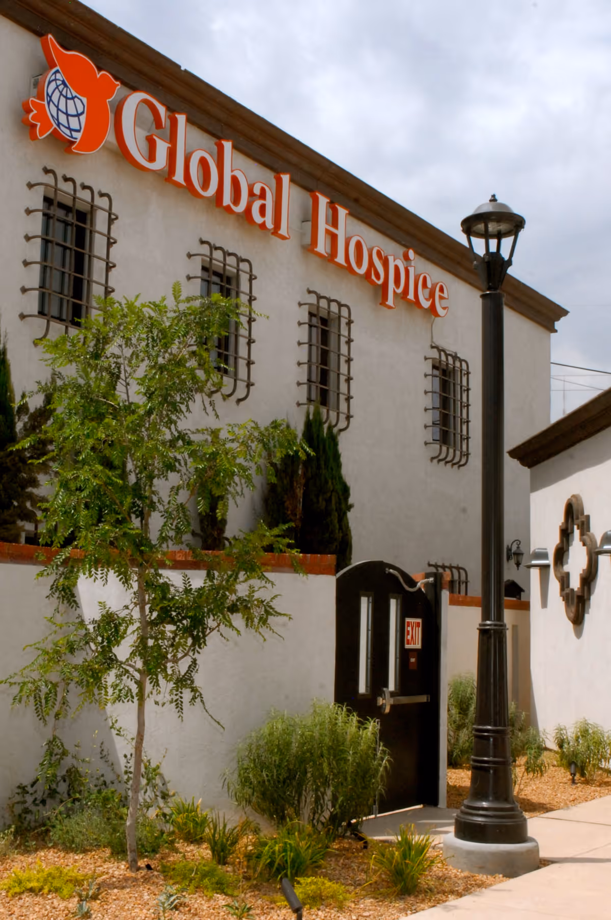 Exterior view of a facility with a Global Hospice Care sign, a lamp post, and landscaping.