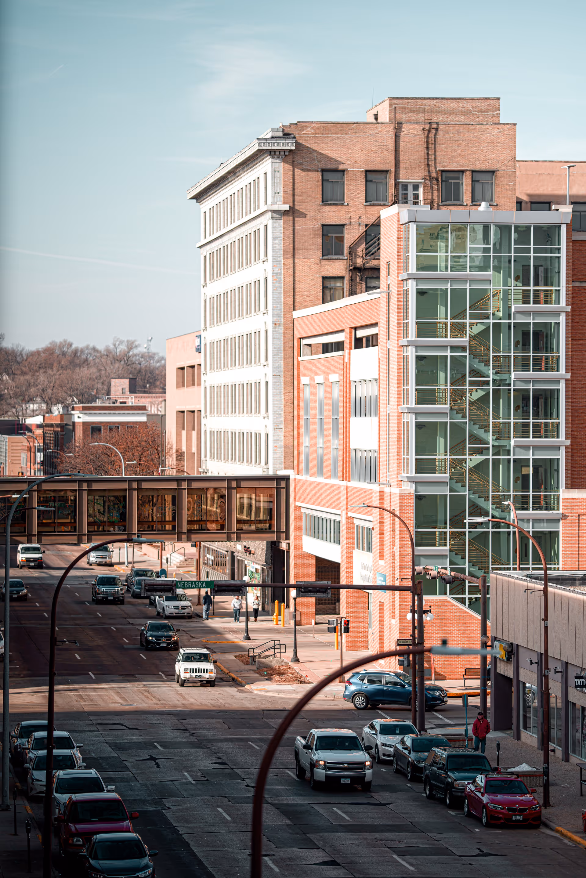 City street with brick buildings, cars, and a glass-enclosed stairwell on a modern facade.