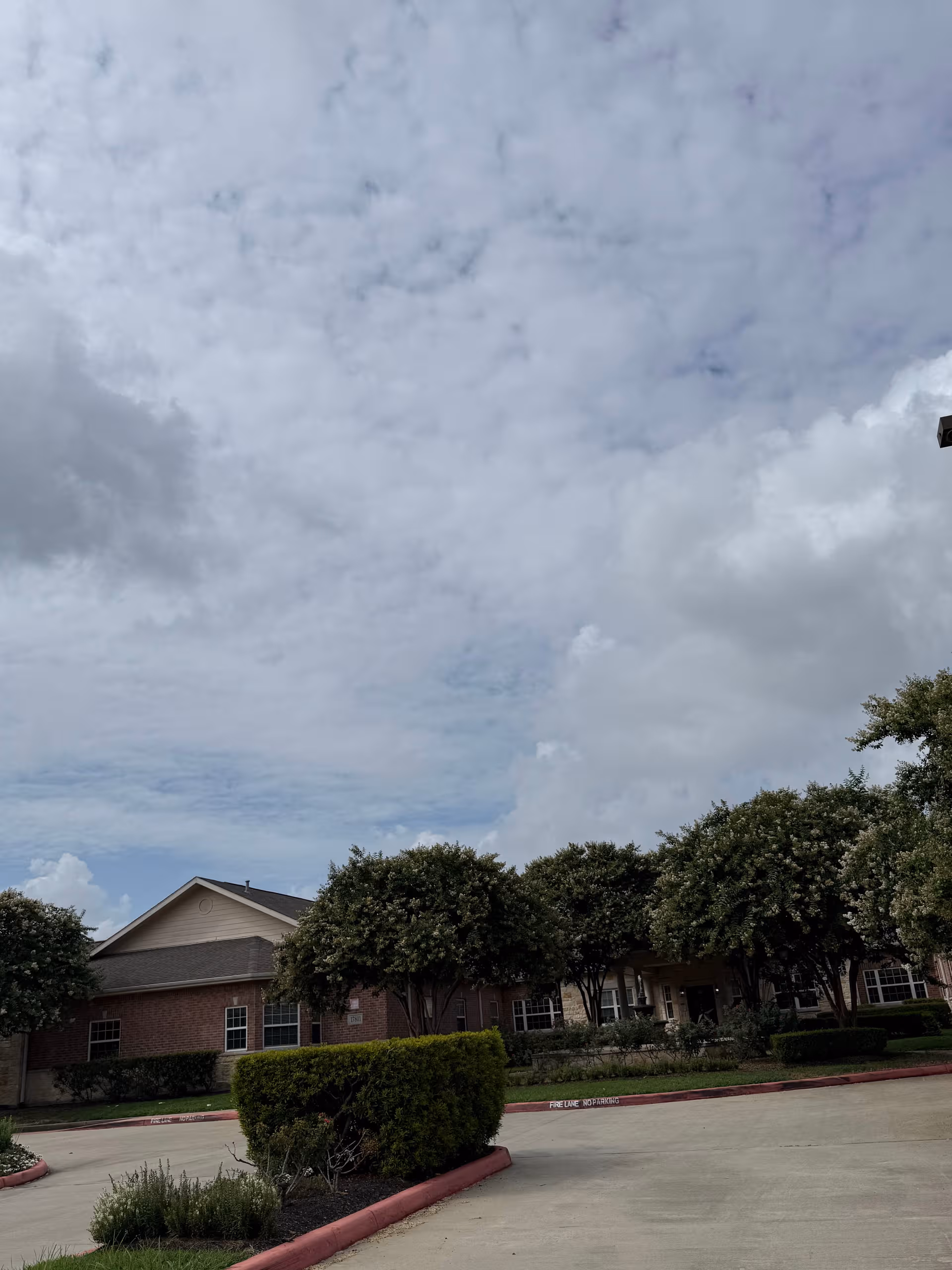 Exterior view of Cypress Assisted Living CyFair building with trees and a driveway.