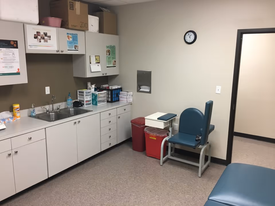 Clinical supply room with sink, cabinets, medical supplies, and a blue patient chair.