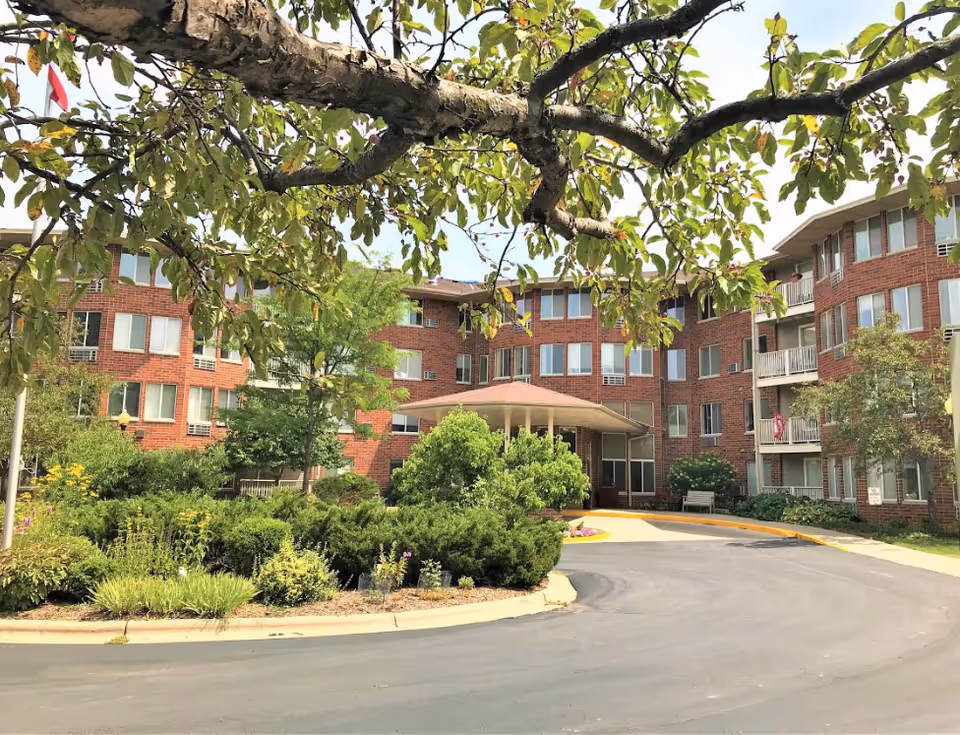 Brick senior living building with curved driveway, front entrance canopy, and landscaped grounds.
