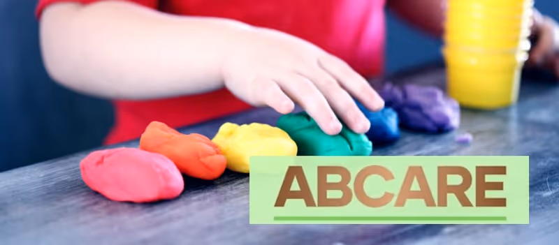 Close-up of colorful clay on a table with a hand and ABCARE logo