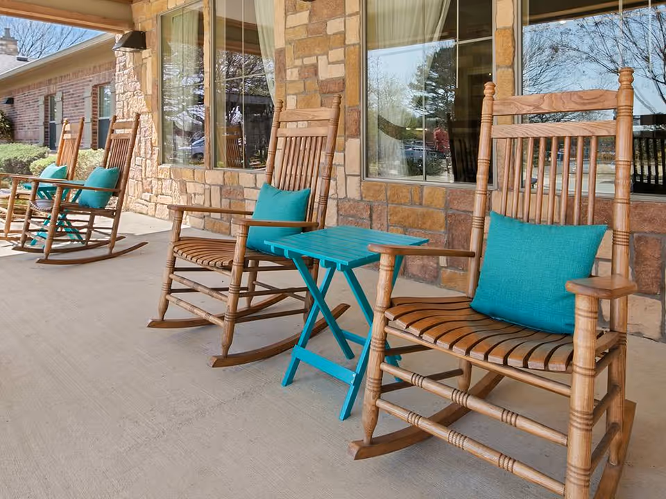 Wooden rocking chairs with teal cushions and a small teal table on a stone-front porch.