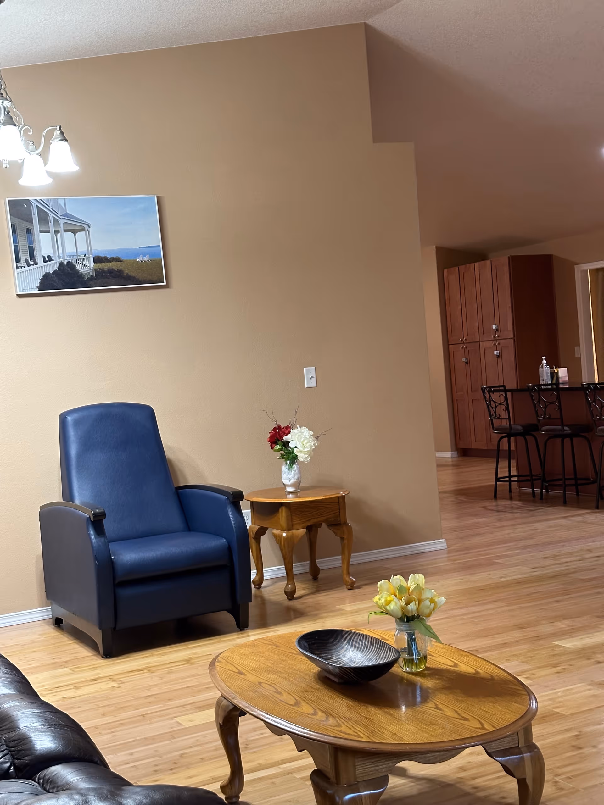 Beige-walled lounge with blue armchair, wooden coffee table, and floral arrangements in a common area.