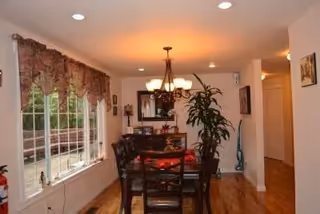 A dining room with a dark wood table, chairs, chandelier, and large windows.